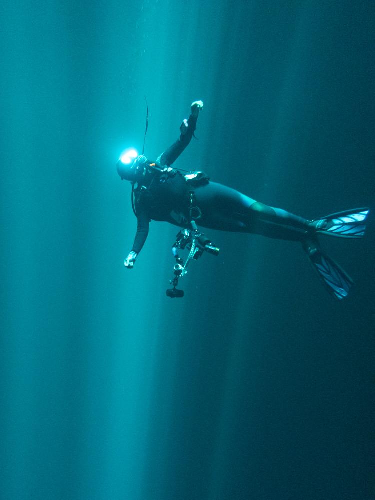 Female scuba diving looking up into a hole with light shining of her mask
